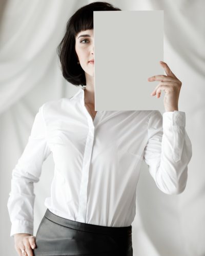 beautiful young woman with dark short hair holding a magazine, book with mock up. girl in a white shirt and black leather skirt standing in studio.